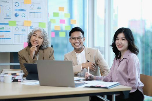 Group of Asia young creative people in smart casual wear smiling in creative office workplace. Diverse Asian male and female stand together at startup. Coworker teamwork concept..