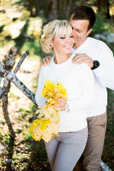 Man hugs woman from behind with a bouquet of yellow leaves in her hands. High quality photo