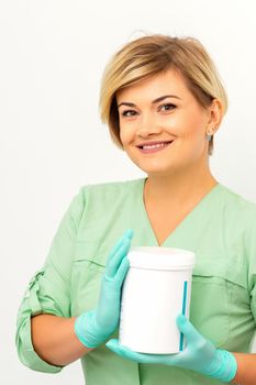 Cosmetics creams and skin care products in the hands of the female beautician smiling and standing over the white wall background