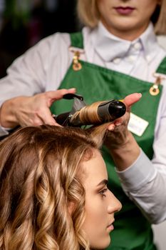 The female hairdresser is curling hair for a brown-haired young caucasian woman in a beauty salon