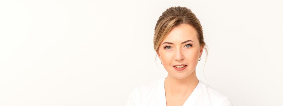 Close-up portrait of young smiling female caucasian healthcare worker standing staring at the camera on white background