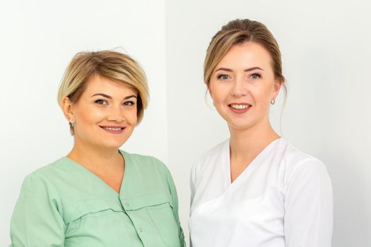 Close-up portrait of two young smiling female caucasian healthcare workers standing staring at the camera on white background