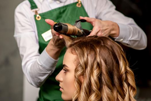 The female hairdresser is curling hair for a brown-haired young caucasian woman in a beauty salon