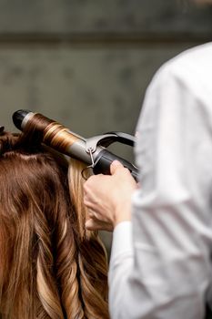 The female hairdresser is curling hair for a brown-haired young caucasian woman in a beauty salon