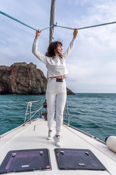 Woman standing on the nose of the yacht at a sunny summer day, breeze developing hair, beautiful sea on background.