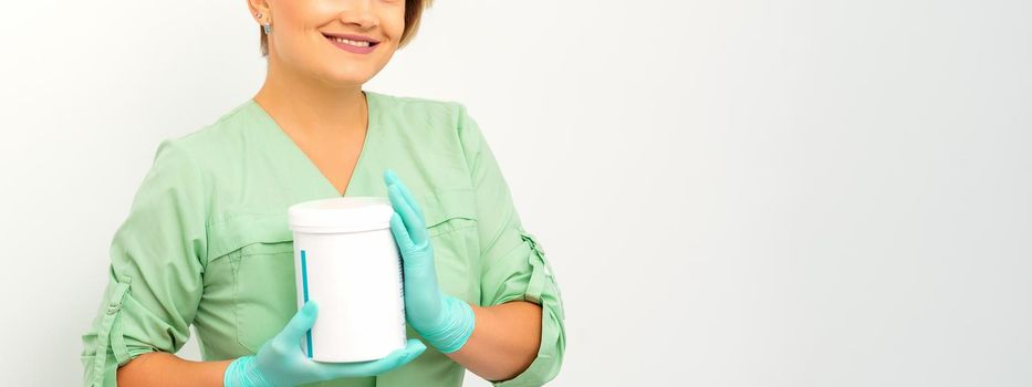 Cosmetics creams and skin care products in the hands of the female beautician smiling and standing over the white wall background