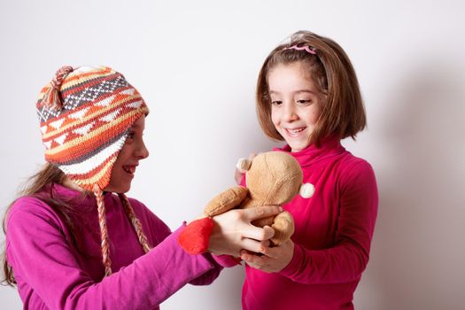 Little girl giving her teddy bear toy to younger sister. Cute child girl giving a gift to her sister. Child girl sharing a toy with a friend