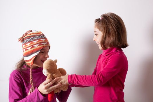 Little girl giving her teddy bear toy to older sister. Cute child girl giving a gift to her sister