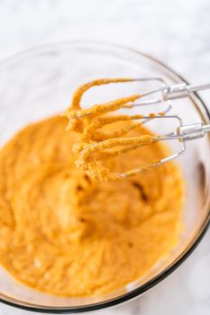 Mixing ingredients in a large glass mixing bowl to bake pumpkin bunt cake.