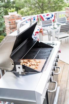Grilling shrimp on a grill mat over an outdoor gas grill.