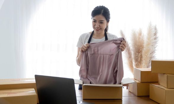 Startup small business entrepreneur SME, asian woman packing shirt in box. Portrait young Asian small business owner home office, online sell marketing delivery, SME e-commerce telemarket job concept.