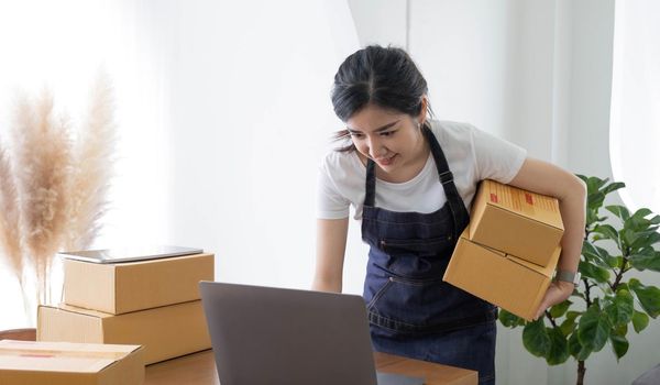 Startup happy Asian woman business owner works with a box at home, prepare parcel delivery SME supply chain, procurement, package box to deliver to customers, Online SME business entrepreneurs ideas,.