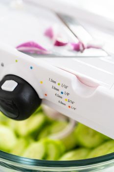 Slicing vegetables on slicer to make summer cucumber salad.