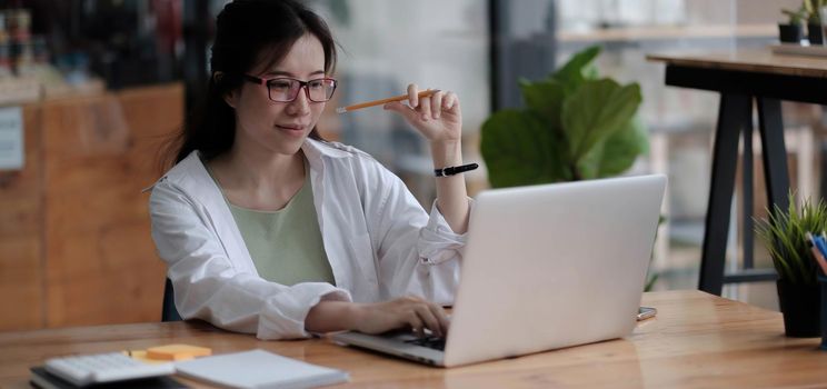 Charming asian businesswoman sitting working on laptop in office..