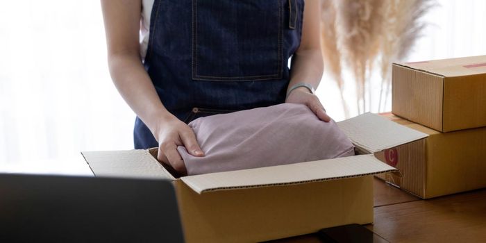 Startup small business entrepreneur SME, asian woman packing shirt in box. Portrait young Asian small business owner home office, online sell marketing delivery, SME e-commerce telemarket job concept.