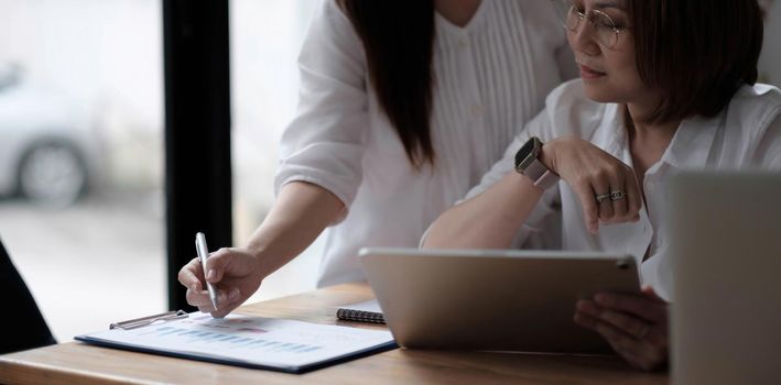 Two women analyzing documents while sitting on a table in office. Woman executives at work in office discussing some paperwork..