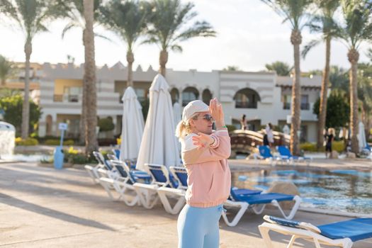 fitness, sport, people and healthy lifestyle concept - woman making yoga in lord of the dance pose on mat over beach and swimming pool background