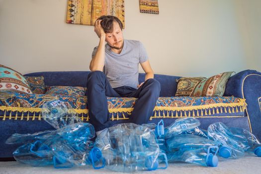 Young caucasian man hamong empty plastic bottles to recycle with sad expression.