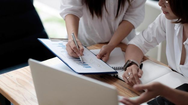 Two women analyzing documents while sitting on a table in office. Woman executives at work in office discussing some paperwork..