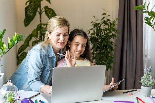 Beautiful young woman and her little cute daughter are using laptop at home. Enjoying spending time together.