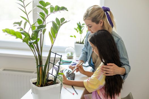 Charming little girl and her beautiful young mom are using a digital tablet and smiling at home.