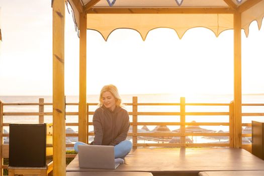 Woman using a laptop at the beach during sunset.