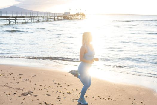 Attractive fit woman practicing side lunges, exercising on the beach on a bright sunny day. Healthy lifestyle, outdoor workout.