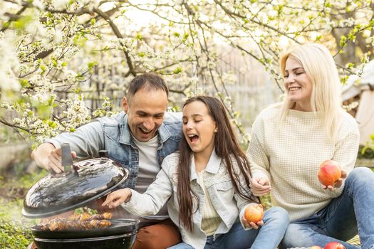 Happy family having a barbecue in their garden in spring. Leisure, food, family and holidays concept