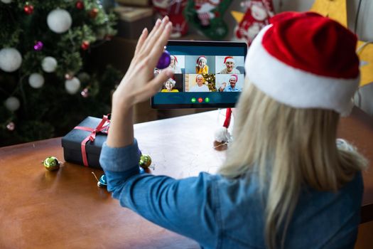 A young woman on the background of a Christmas tree with gifts, with a tablet has a video call or video chat with friends, family. Christmas online holiday. Stay home vacation.