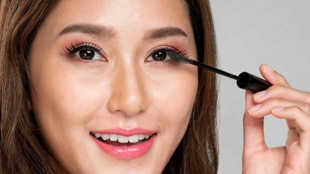 Closeup ardent young woman putting mascara on her long eyelashes with brush. Beauty cosmetic concept. Female model with perfect skin.