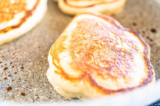 Frying kefir based pancakes in cooking pan on an electric stove.