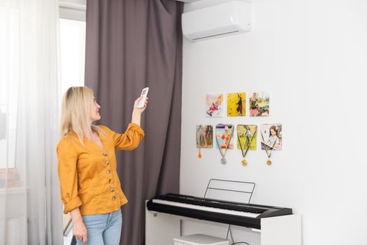 Portrait Of Smiling Young Woman Holding Remote Controller Of Air Conditioner At Home
