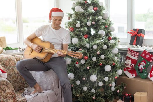 young handsome man sitting on the sofa, he is playing guitar, music, christmas, relax concept.