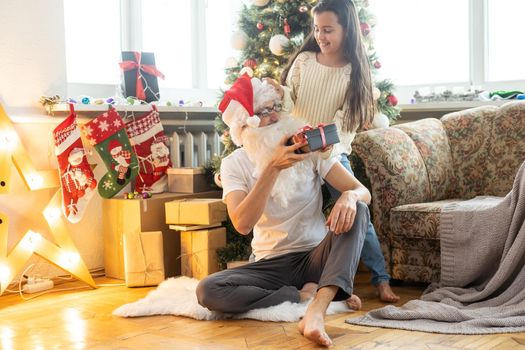 Picture of happy family celebrating New Year eve, little girl with parents enjoying winter holidays, father wearing Santa Claus costume, Christmas magic, happiness and love concept.