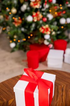 Beautiful Christmas gift boxes with red ribbon and pine cones on the table near the tree in the room