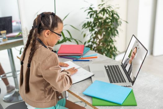 Child online. A little girl uses a laptop video chat to communicate learning while sitting at a table at home