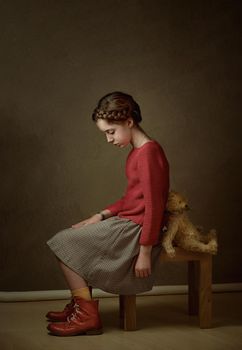 a girl with dark hair and a pigtail around her head in a red sweater is sitting with her teddy bear toy back to back offended at each other. High quality photo