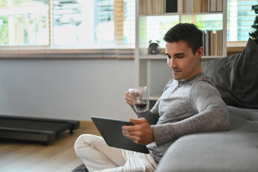 Young man drinking hot coffee and reading news on digital tablet in the morning.