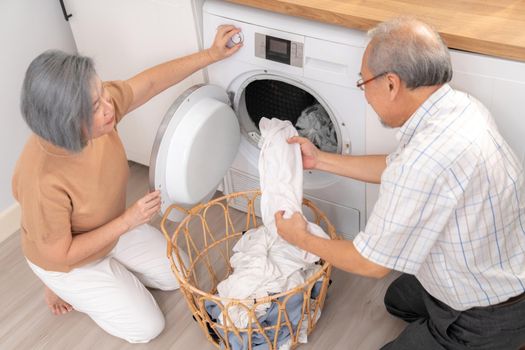 Senior couple working together to complete their household chores at the washing machine in a happy and contented manner. Husband and wife doing the usual tasks in the house.