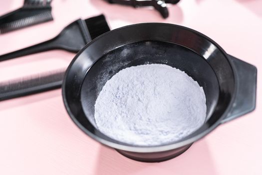 Hair color dye powder in a black plastic mixing bowl on a pink background.