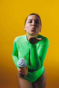 A smiling woman in a green swimsuit with a cocktail in her hands is happy about the upcoming vacation, isolated on a bright yellow background. Summer tropics travel concept.