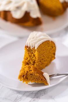 Slice of homemade pumpkin bunt cake with cream cheese frosting on a white plate.