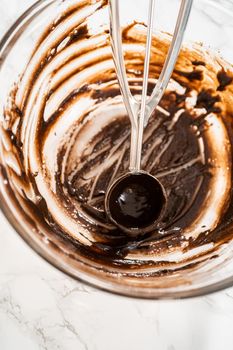 Scooping cake batter with dough scoop into cupcake foil liners to bake chocolate peppermint cupcakes.