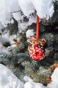 Red christmas ball hanging on spruce tree branches covered with snow. Green spruce tree and red toy ball in winter city park. Christmas or New year's composition.
