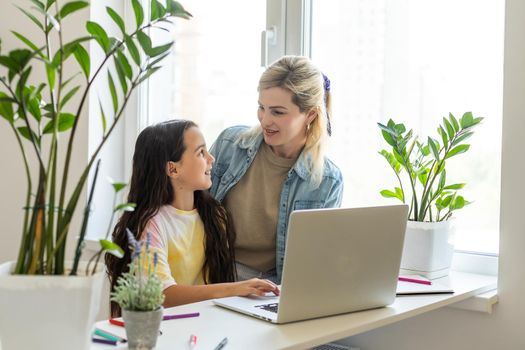 Happy mother with little kid daughter having fun online with application, watching video cartoons or playing game on laptop together, young babysitter or nanny teaching child girl to use computer.