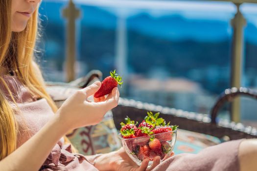 Portrait of gorgeous woman wearing beautiful dress sitting in a patio and eating strawberry.
