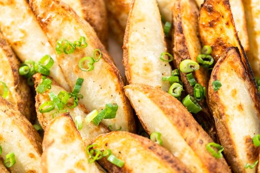 Freshly baked potato wedges with spices on a white serving tray.