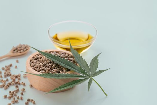 CBD oil, THC tinture in glass bowl and bottle with dropper lid and hemp leaf on empty background with a pile of dry hemp seeds surrounded in minimalism. Legalized marijuana concept.