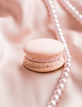 Girly, bakery and branding concept - Sweet macaroons and pearls jewellery on silk background, parisian chic jewelry, French dessert food and cake macaron for luxury confectionery brand, holiday gift