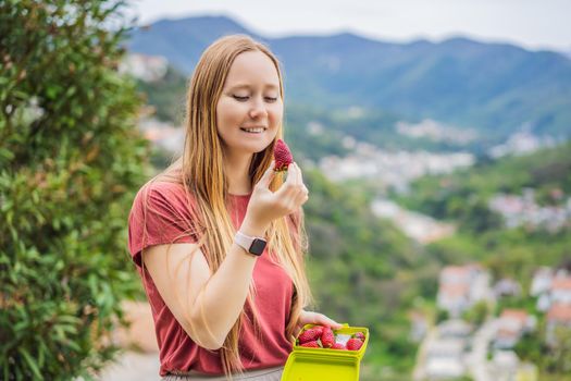 Young attractive woman eating a strawberry, outdoors.